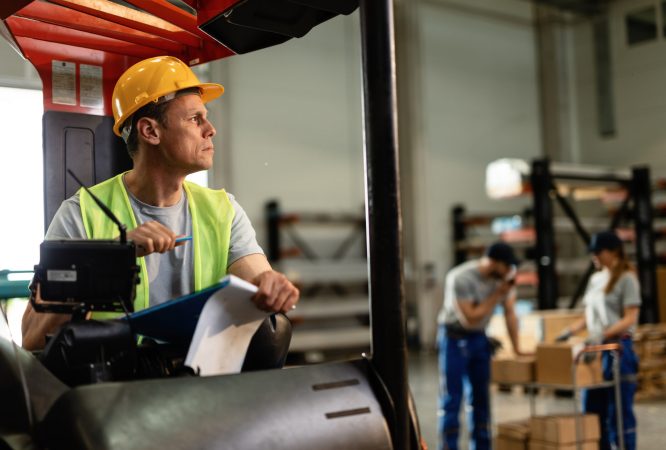 Forklift driver going through paperwork and thinking of something while working in distribution warehouse.