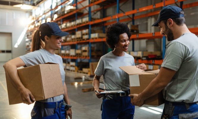 Happy African American woman and her coworkers examining packages while working in distribution warehouse.