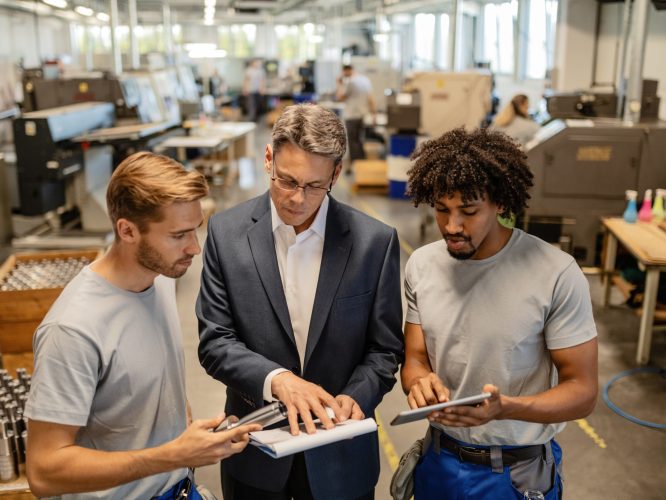 Mid adult engineer and two steel workers going through quality reports while working in industrial building.