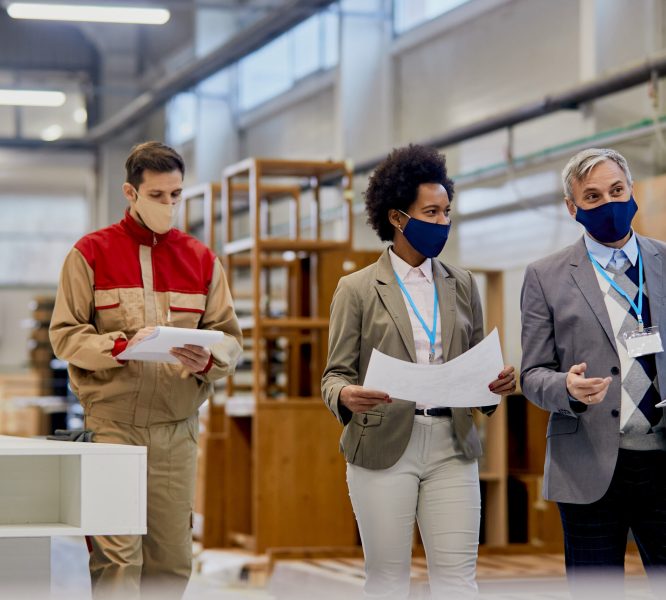 Company managers with protective face masks talking while visiting wood factory facility.